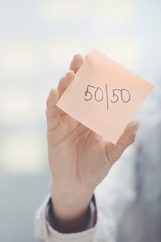 Hands holding sticky note with Fifty-fifty text 