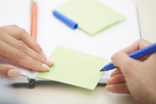 Hands of woman writing on adhesive note with empty space