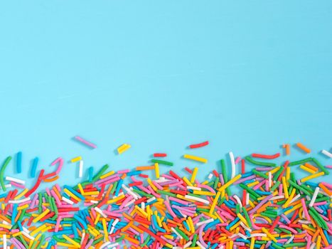 Border frame of colorful sprinkles on blue background with copyspace. Top view or flat lay