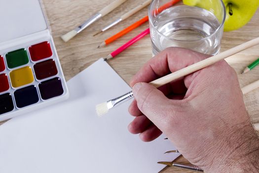 The artist’s hand drawing a paint, brushes and pencils. Art background