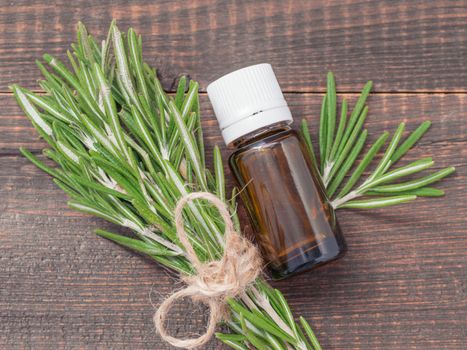 Rosemary essential oil in dark glass bottle and fresh rosemary on dark wooden background. Top view or flat lay