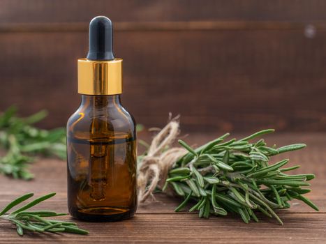 Rosemary essential oil in dark glass bottle and fresh rosemary on dark wooden background with copy space