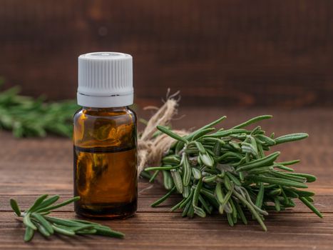 Rosemary essential oil in dark glass bottle and fresh rosemary on dark wooden background with copy space