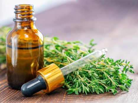 thyme essential oil and dark glass bottle with pipette and fresh thyme on dark brown wooden background with copy space