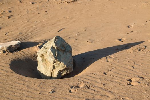 Sandy beach in an early morning light. Big stone with a long shadow. Waves from the wind and water in the sand. Sidi Ifni, Morocco