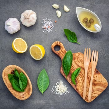 The ingredients for homemade pesto sauce. Various herbs sweet basil, parmesan cheese ,garlic, olive oil , lemon and himalayan salt over dark concrete background flat lay.