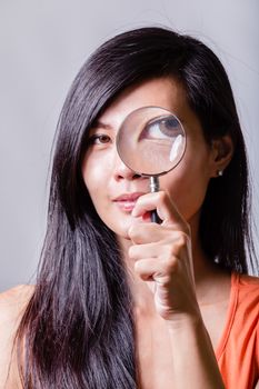 Asian woman holding magnifying glass to eye