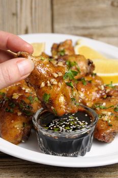 Fried chicken wing in ginger garlic marinade with herbs in hand over soy sauce