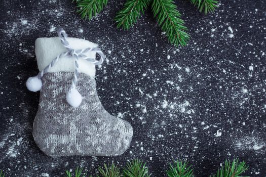 Christmas and New Year winter holiday snowbound composition of grey stocking on black space background with green fir tree branches