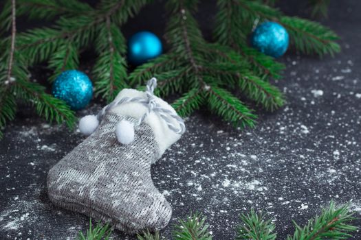 Christmas and New Year winter holiday snowbound composition of grey stocking on black space background with green fir tree branches and blue balls ornament