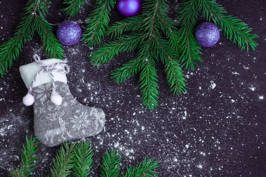 Christmas and New Year winter holiday snowbound composition of grey stocking on black space background with green fir tree branches and purple balls ornament