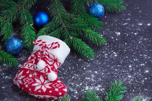 Christmas and New Year winter holiday snowbound composition of red stocking on black space background with green fir tree branches and blue balls ornament