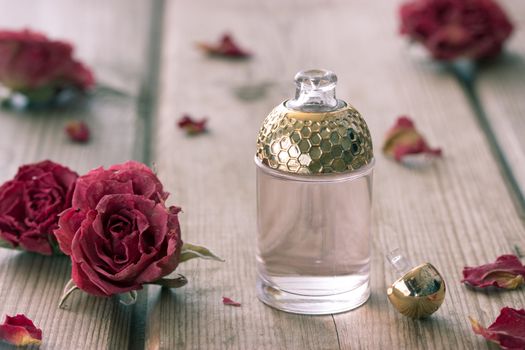 perfume bottle and dry roses on wooden table