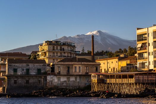 View of the volcano Etna from a small fishing village illuminated by the afternoon sun