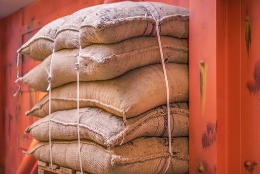 Cropped image with a pile of burlap bags full of goods, stacked on a pallet in a storage and ready for shipment.