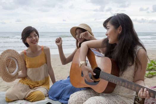 younger asian woman friend vacation relaxing playing guitar and sing a song on sea beach