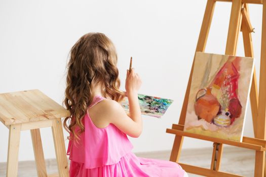 Portrait of a lovely little girl painting a picture in a studio or art school. Creative pensive painter child paints a colorful picture on canvas with oil colors in workshop. Talented kids