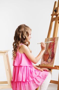 Portrait of a lovely little girl painting a picture in a studio or art school. Creative pensive painter child paints a colorful picture on canvas with oil colors in workshop. Talented kids