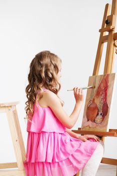 Portrait of a lovely little girl painting a picture in a studio or art school. Creative pensive painter child paints a colorful picture on canvas with oil colors in workshop. Talented kids