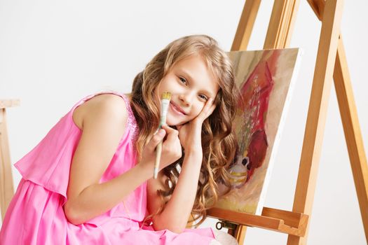 Portrait of a lovely little girl painting a picture in a studio or art school. Creative pensive painter child paints a colorful picture on canvas with oil colors in workshop. Talented kids