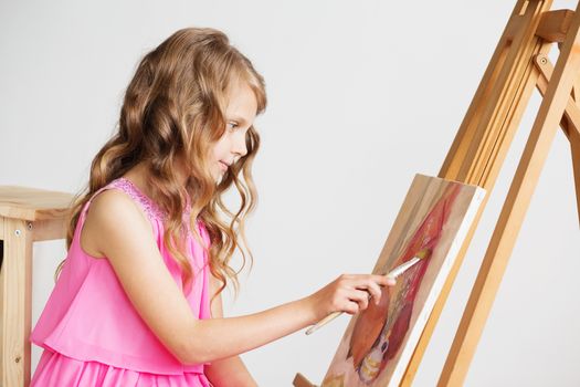 Portrait of a lovely little girl painting a picture in a studio or art school. Creative pensive painter child paints a colorful picture on canvas with oil colors in workshop. Talented kids