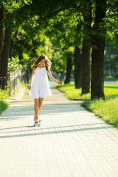 lovely urban woman in white dress with a pink skate. Young girl riding in the park on a skateboard