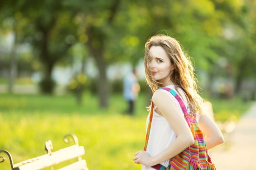 Portrait of lovely urban girl with backpack in the street. Happy smiling woman. Fashionable blonde girl walking in a city park