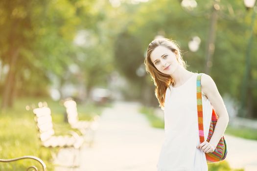 Portrait of lovely urban girl with backpack in the street. Happy smiling woman. Fashionable blonde girl walking in a city park