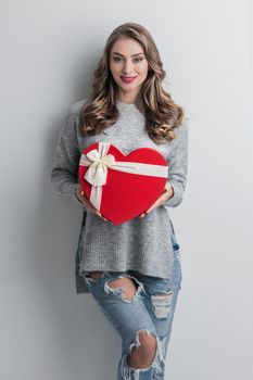 Young girl with red heart-shaped gift box on white background