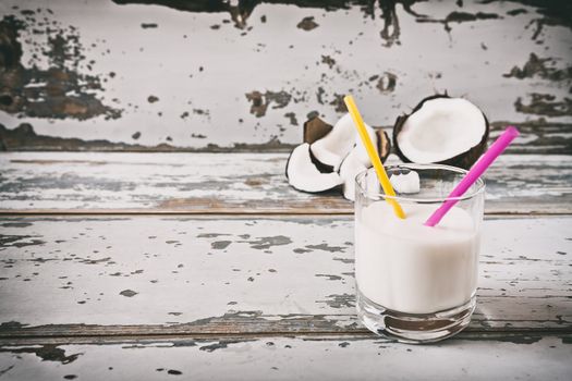 Coconut milk in a glass and a broken coconut on background over an old table