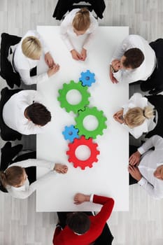 Business team sitting around the table with cogs, teamwork concept