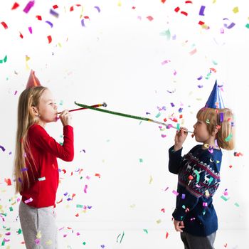 Children blowing party trumpets with confetti celebrating new year