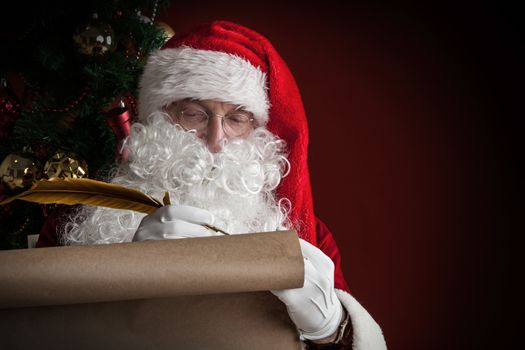 Santa Claus writing on old paper roll list with quill pen