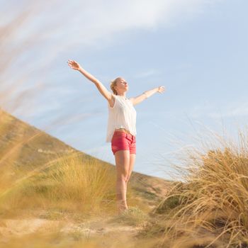 Relaxed woman, arms rised, enjoying sun, freedom and life an a beautiful beach. Young lady feeling free, relaxed and happy. Concept of vacations, freedom, happiness, enjoyment and well being.