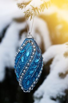 Blue Christmas ball hanging on natural branch of pine in snowy weather.