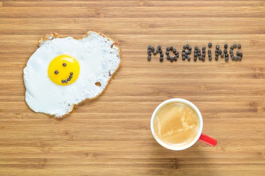 Smiling fried egg lying on a white plate on a wooden cutting board with silver fork near it. Classic Breakfast concept
