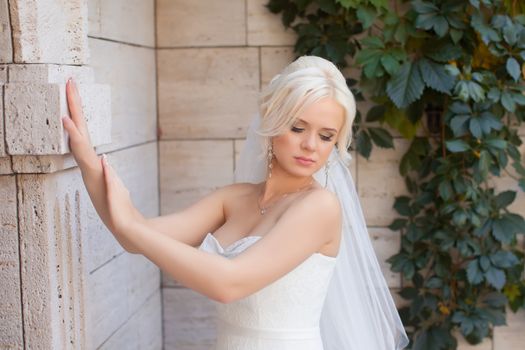 The blonde bride standing at the wall, posing in the photo