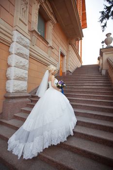 Bride in wedding dress with long train climbs the stairs