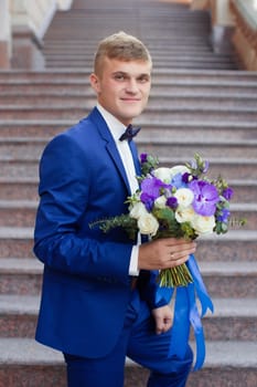 The groom in a blue suit with a bouquet on the steps