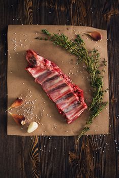 Uncooked pork ribs on paper with thyme and garlic, wooden background