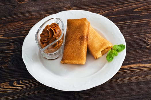 Pancakes with condensed milk on a plate, wooden background