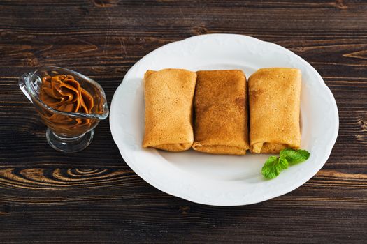 Pancakes with condensed milk on a plate, wooden background