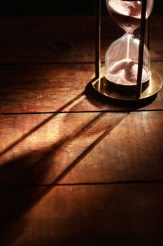 Vintage hourglass on wooden background with long shadow