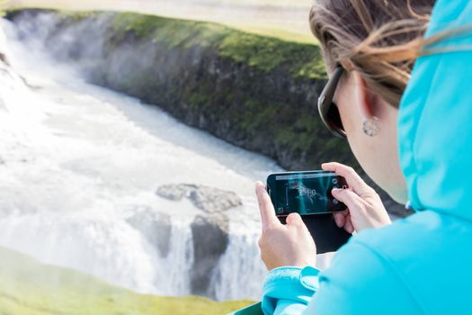 Woman photographing a waterfall with a mobile phone - Iceland