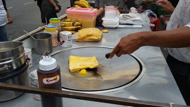 Bangkok, Thailand - October 30, 2016: Chef are cooking roti for sale to customer on the food wagon. Using butter, sugar, banana, sweetened condensed milk and chocolate as an ingredients. Roti is the Indian style oily appetizer, cooking with oil, butter and vary topping such as eggs, banana, sweetened condensed milk etc. Very popular among Thai people.