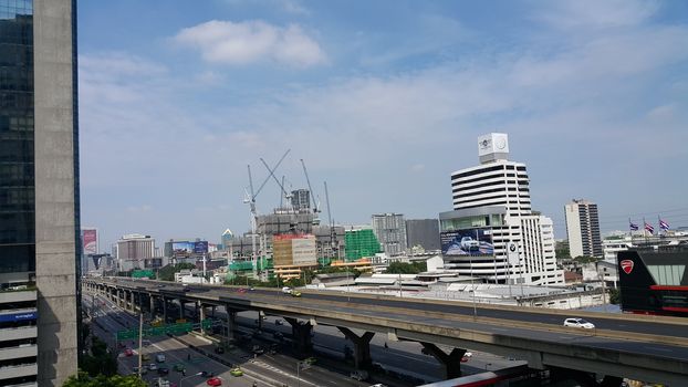 Bangkok, Thailand - November 04, 2016: People are moving on their vehicle on both express way and normal way. The photo also shown the sign of bank branch, the under-construction building with working crane, the car showroom and the motorcycle showroom.
