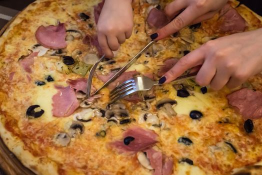 children hands cut pizza on wooden board