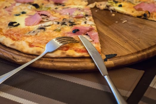 fork, knife and pizza on a wooden cutting board