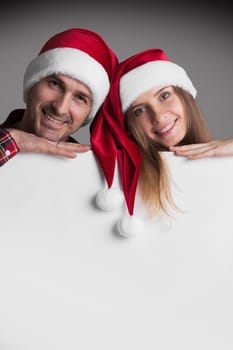 Happy smiling couple in Santa's hats with white blank banner with copy space