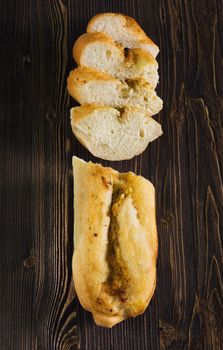 Top view of a sliced of baguette with herbs and spice, dark wooden background